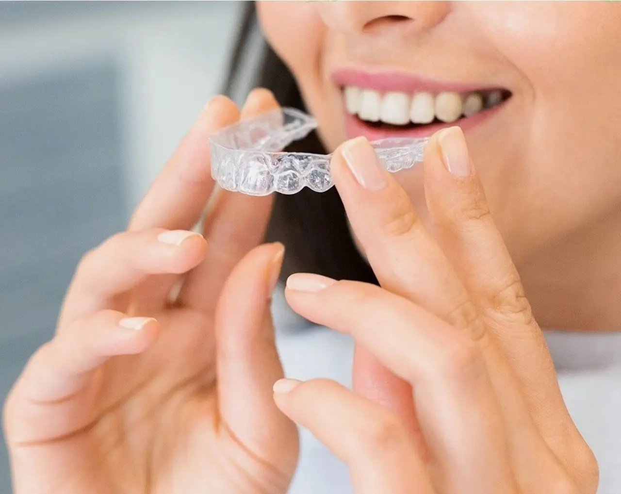 A person smiling while holding a clear aligner tray